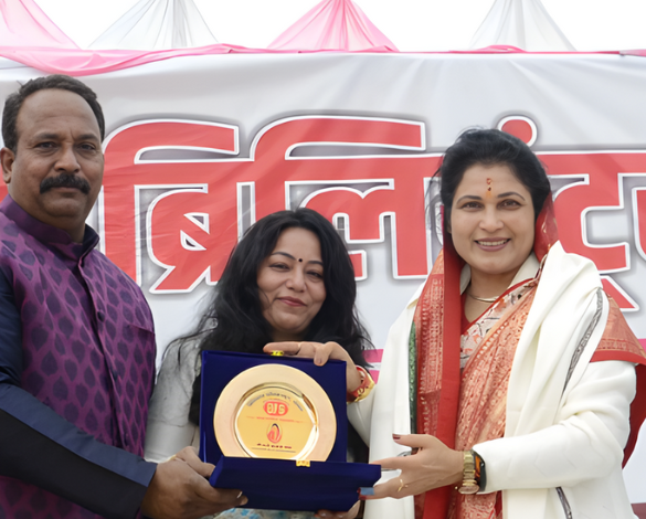 Three people presenting an award plaque at a public event, smiling in front of a banner.